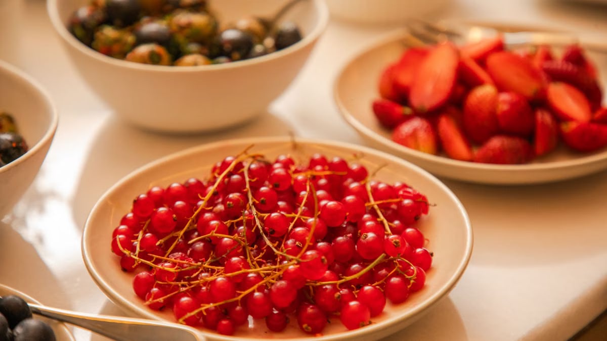 A vibrant display of fresh berries including red currants, strawberries, and grapes artfully arranged on a table.