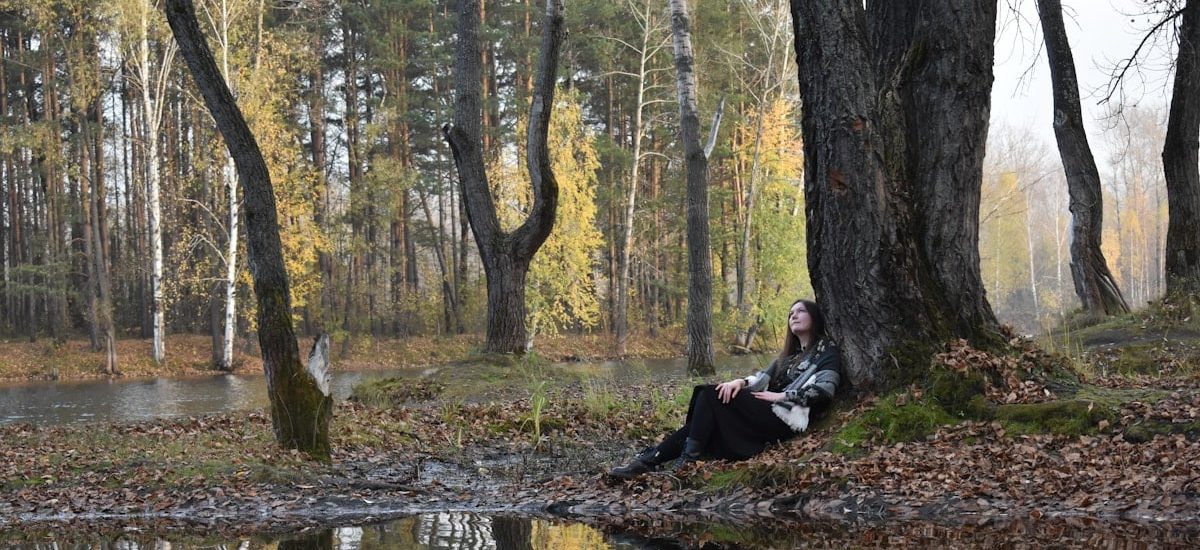 Woman resting under a tree by a reflective lake.