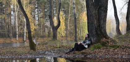 Woman resting under a tree by a reflective lake.