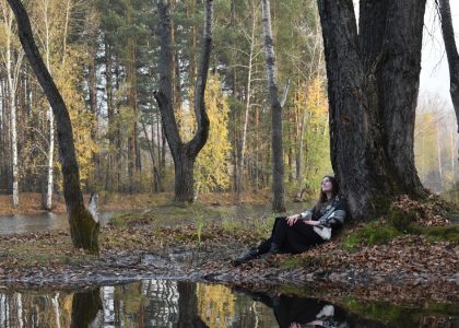 Woman resting under a tree by a reflective lake.